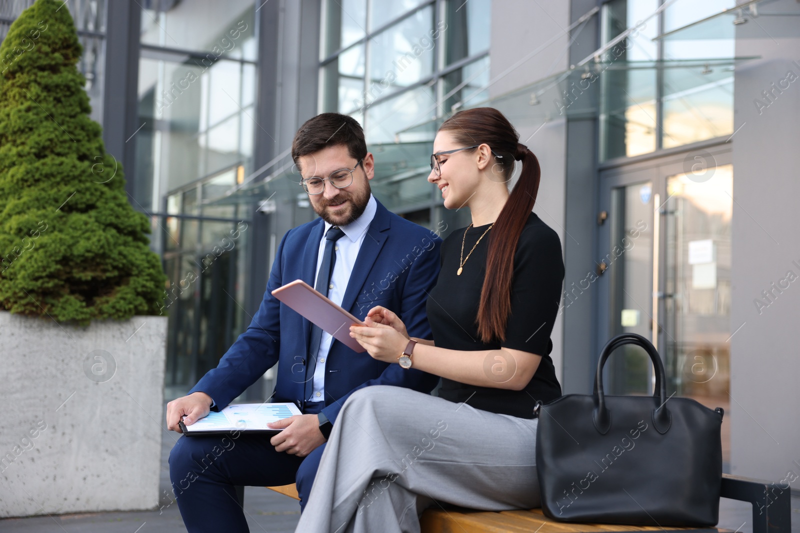 Happy coworkers with tablet discussing something near office building Photo of Happy coworkers with tablet discussing something near office building