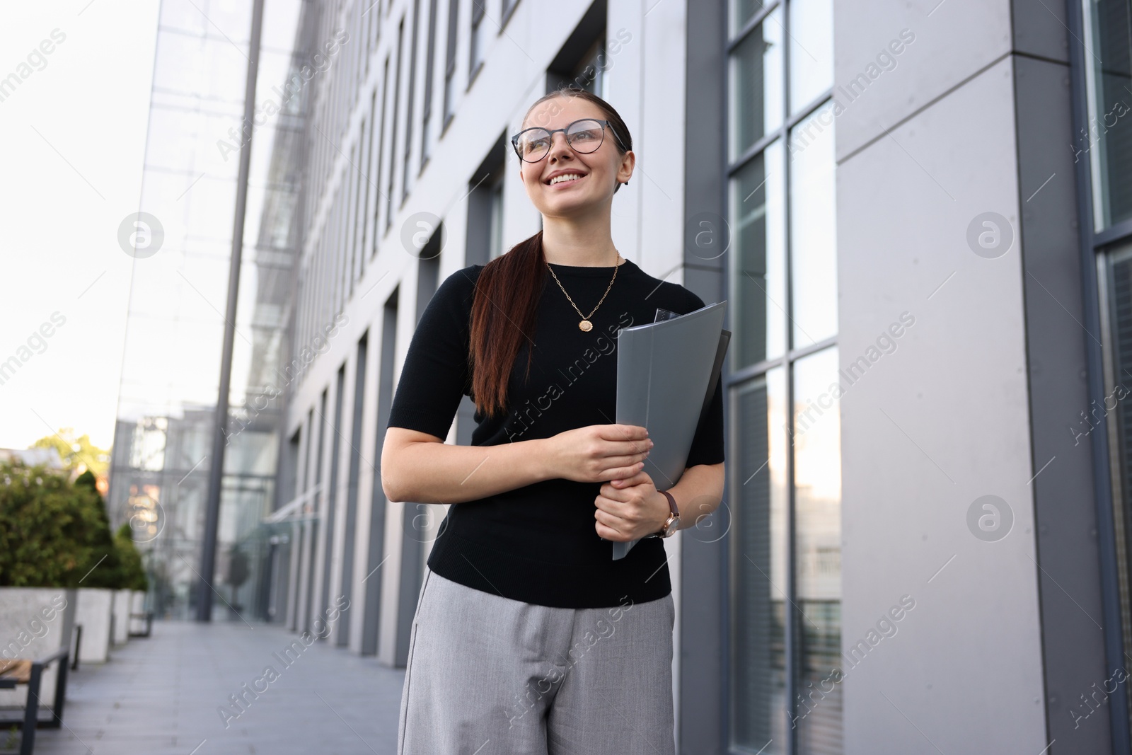Successful businesswoman with folder near office building Photo of Successful businesswoman with folder near office building