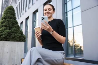 Photo of Successful businesswoman with coffee and smartphone near office building