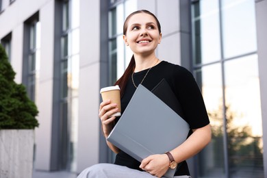 Photo of Successful businesswoman with coffee and folder near office building