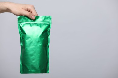 Photo of Woman holding blank zipper stand-up pouch on light grey background, closeup. Space for text