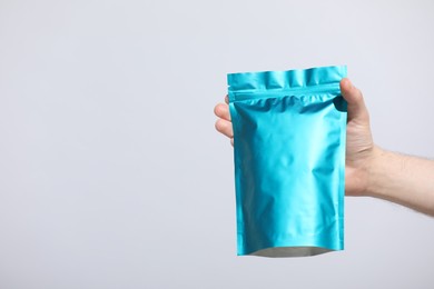 Photo of Woman holding blank zipper stand-up pouch on light grey background, closeup. Space for text