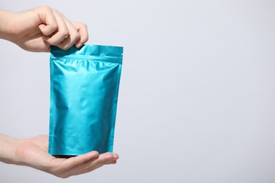 Photo of Woman holding blank zipper stand-up pouch on light grey background, closeup. Space for text
