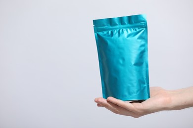 Photo of Woman holding blank zipper stand-up pouch on light grey background, closeup. Space for text