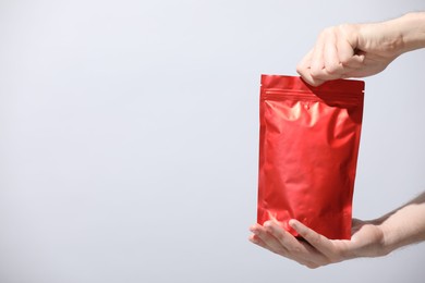 Photo of Woman holding blank zipper stand-up pouch on light grey background, closeup. Space for text