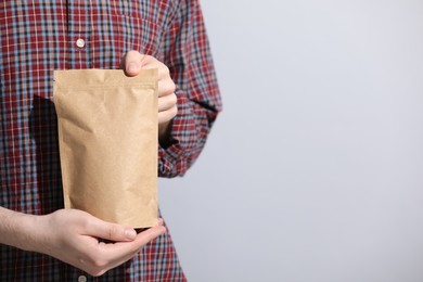 Photo of Woman holding blank zipper stand-up pouch on light grey background, closeup. Space for text