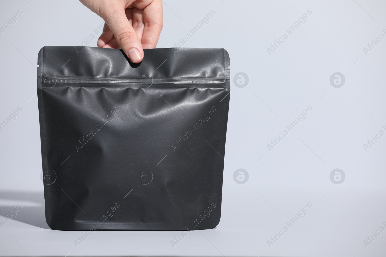 Woman holding blank zipper stand-up pouch on light grey background, closeup. Space for text Photo of Woman holding blank zipper stand-up pouch on light grey background, closeup. Space for text