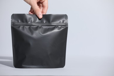 Photo of Woman holding blank zipper stand-up pouch on light grey background, closeup. Space for text