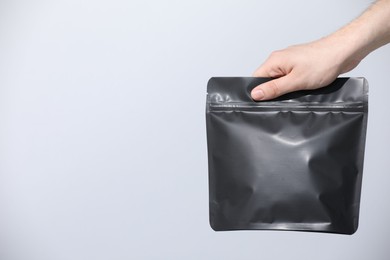 Photo of Woman holding blank zipper stand-up pouch on light grey background, closeup. Space for text