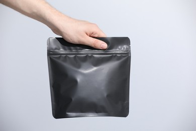 Photo of Woman holding blank zipper stand-up pouch on light grey background, closeup. Space for text