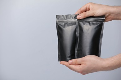 Photo of Woman holding blank zipper stand-up pouches on light grey background, closeup. Space for text