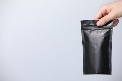 Photo of Woman holding blank zipper stand-up pouch on light grey background, closeup. Space for text