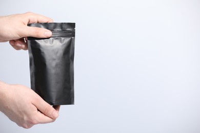 Photo of Woman holding blank zipper stand-up pouch on light grey background, closeup. Space for text
