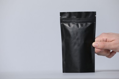 Photo of Woman holding blank zipper stand-up pouch on light grey background, closeup. Space for text