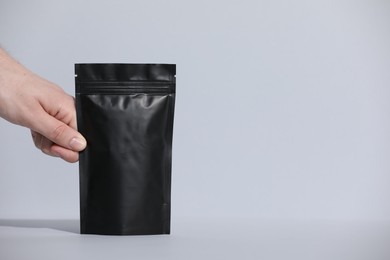 Photo of Woman holding blank zipper stand-up pouch on light grey background, closeup. Space for text