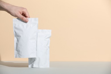 Photo of Woman holding blank zipper stand-up pouches at grey table against beige background, closeup. Space for text