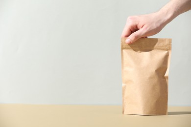 Photo of Woman holding blank zipper stand-up pouch on beige table against light grey background, closeup. Space for text