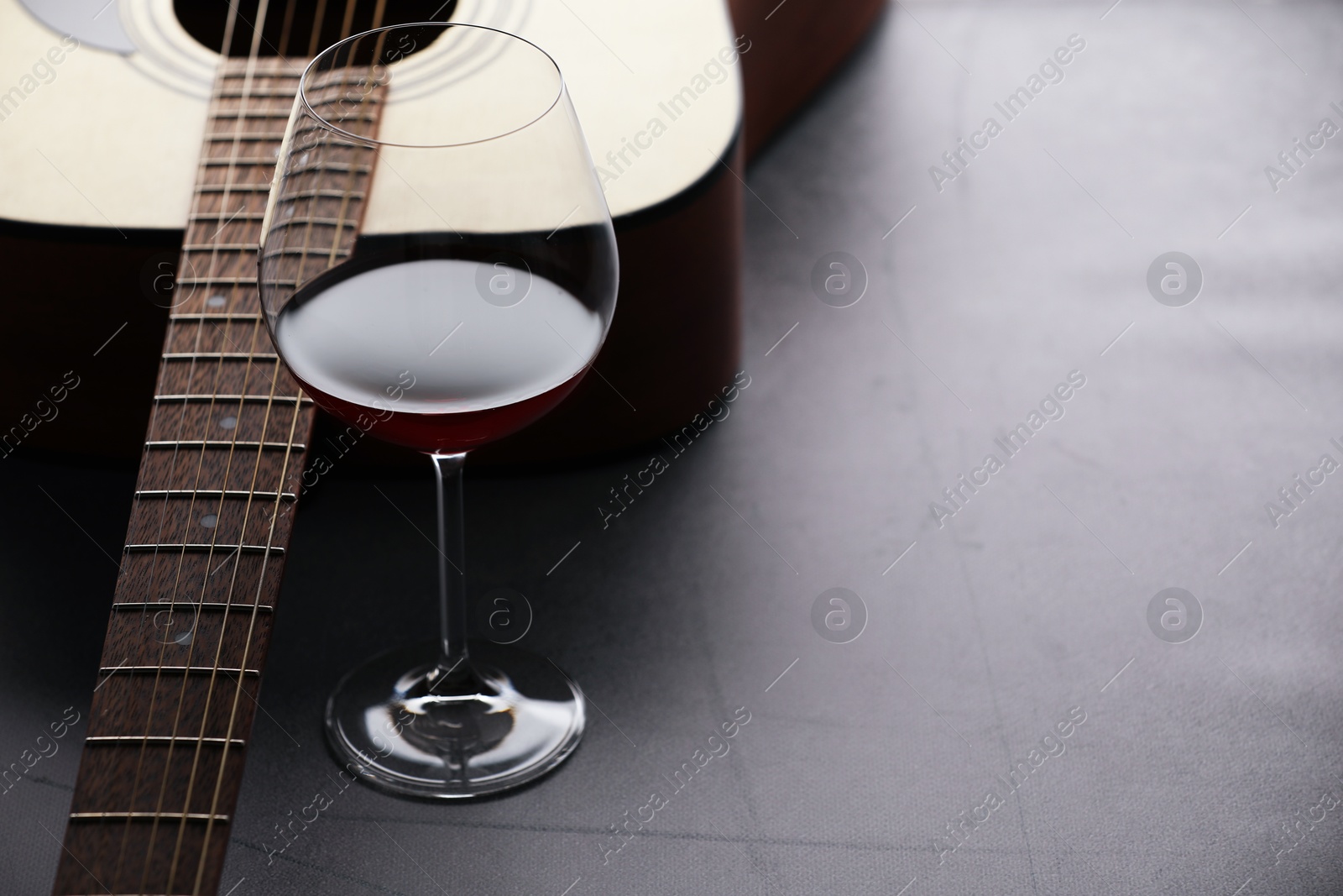 Acoustic guitar and red wine on grey table, closeup. Space for text Photo of Acoustic guitar and red wine on grey table, closeup. Space for text