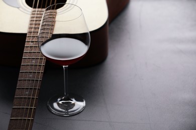 Photo of Acoustic guitar and red wine on grey table, closeup. Space for text