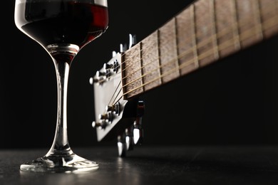 Photo of Acoustic guitar and glass of red wine on black table, closeup