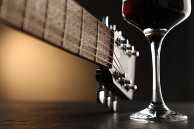 Photo of Acoustic guitar and glass of red wine on black table, closeup
