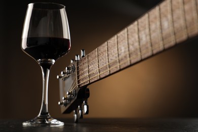 Photo of Acoustic guitar and glass of red wine on black table, closeup