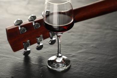 Photo of Acoustic guitar and glass of red wine on black table, closeup