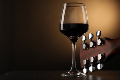 Photo of Acoustic guitar and glass of red wine on black table, closeup. Space for text
