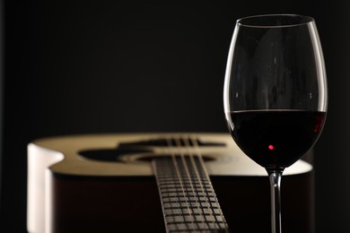Photo of Acoustic guitar and glass of red wine on black background, closeup. Space for text