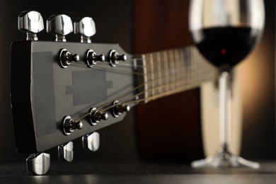Photo of Acoustic guitar and glass of red wine on black table, closeup
