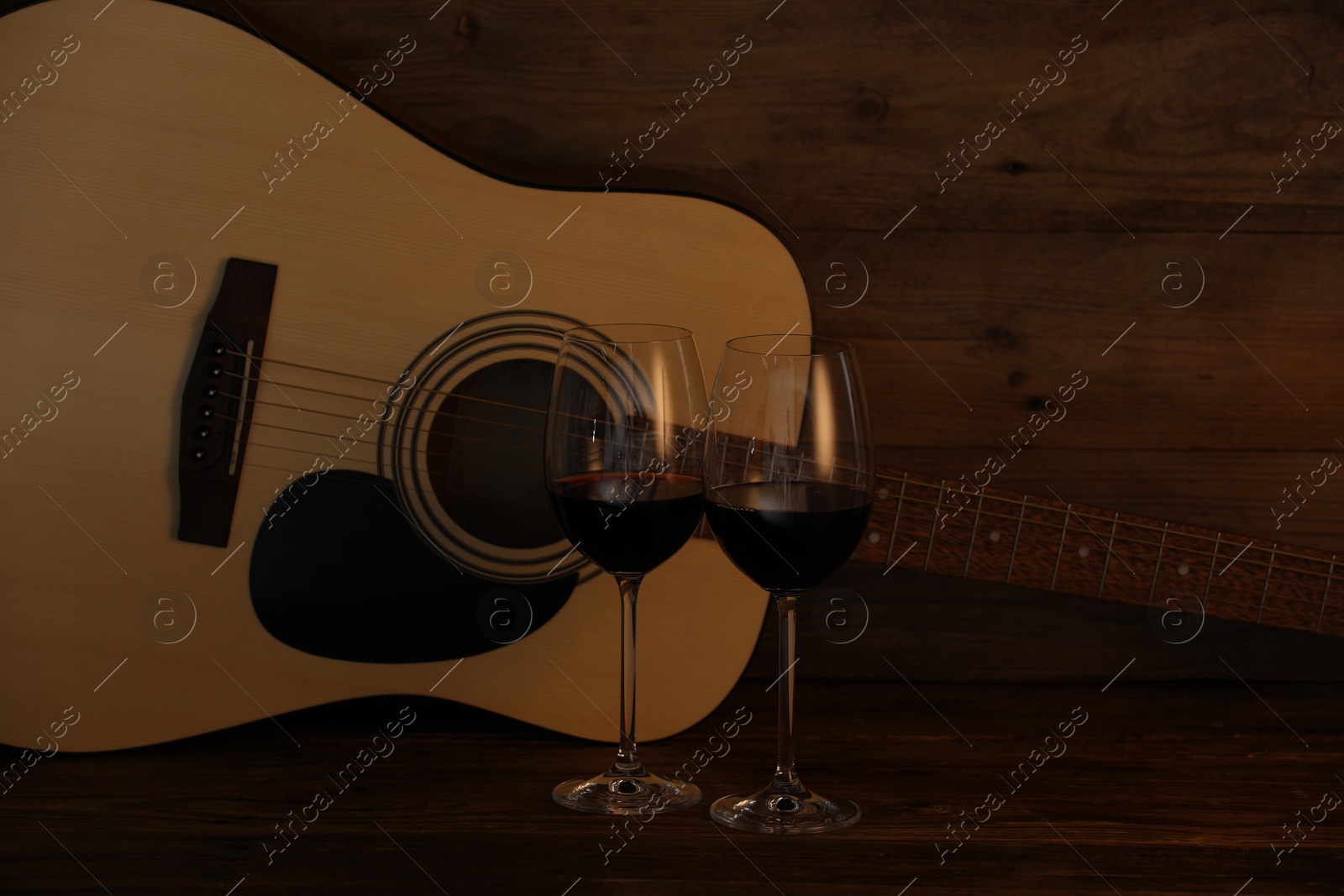 Acoustic guitar and glasses of red wine on wooden table Photo of Acoustic guitar and glasses of red wine on wooden table