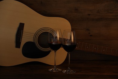Photo of Acoustic guitar and glasses of red wine on wooden table