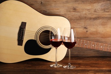 Photo of Acoustic guitar and glasses of red wine on wooden table