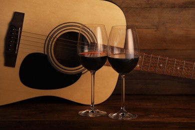 Photo of Acoustic guitar and glasses of red wine on wooden table