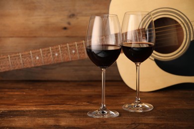 Photo of Acoustic guitar and glasses of red wine on wooden table. Space for text