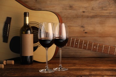 Photo of Acoustic guitar, bottle and glasses of red wine on wooden table. Space for text