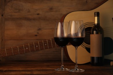 Photo of Acoustic guitar, bottle and glasses of red wine on wooden table. Space for text