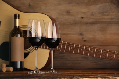 Photo of Acoustic guitar, bottle and glasses of red wine on wooden table. Space for text