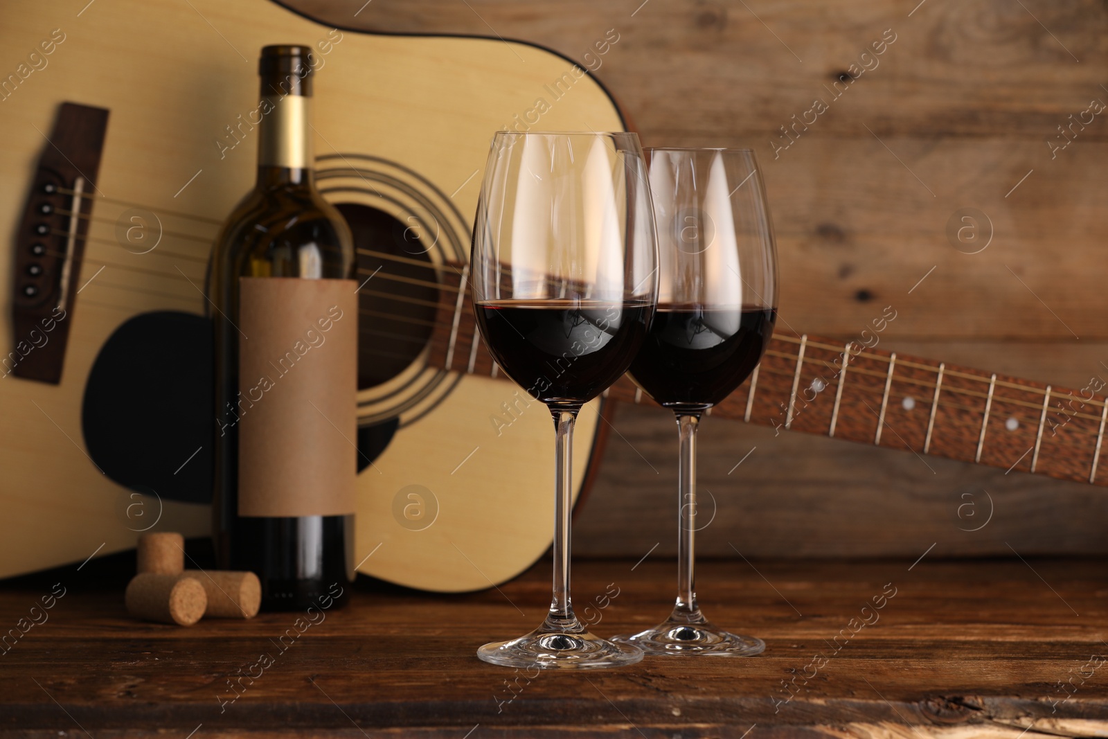 Acoustic guitar, bottle and glasses of red wine on wooden table Photo of Acoustic guitar, bottle and glasses of red wine on wooden table