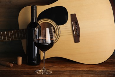 Photo of Acoustic guitar, bottle and glass of red wine on wooden table