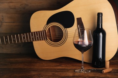 Photo of Acoustic guitar, bottle and glass of red wine on wooden table