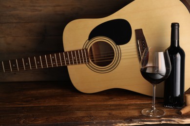 Photo of Acoustic guitar, bottle and glass of red wine on wooden table