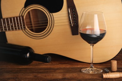 Photo of Acoustic guitar, bottle and glass of red wine on wooden table