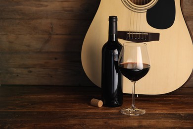 Photo of Acoustic guitar, bottle and glass of red wine on wooden table. Space for text