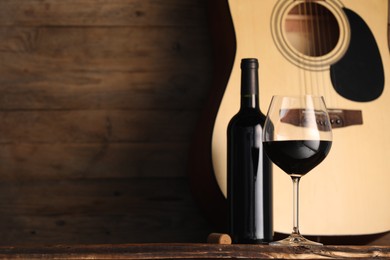 Photo of Acoustic guitar, bottle and glass of red wine on wooden table. Space for text
