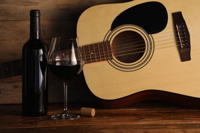 Photo of Acoustic guitar, bottle and glass of red wine on wooden table