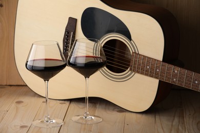 Photo of Acoustic guitar and glasses of red wine on wooden table