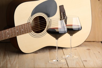 Photo of Acoustic guitar and glasses of red wine on wooden table