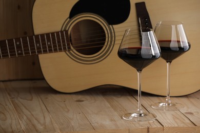 Photo of Acoustic guitar and glasses of red wine on wooden table. Space for text