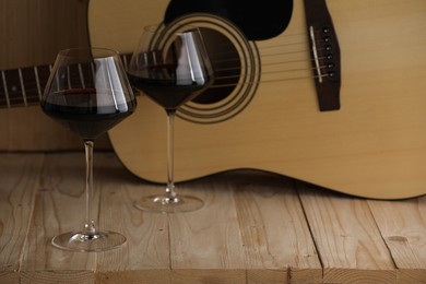 Photo of Acoustic guitar and glasses of red wine on wooden table. Space for text